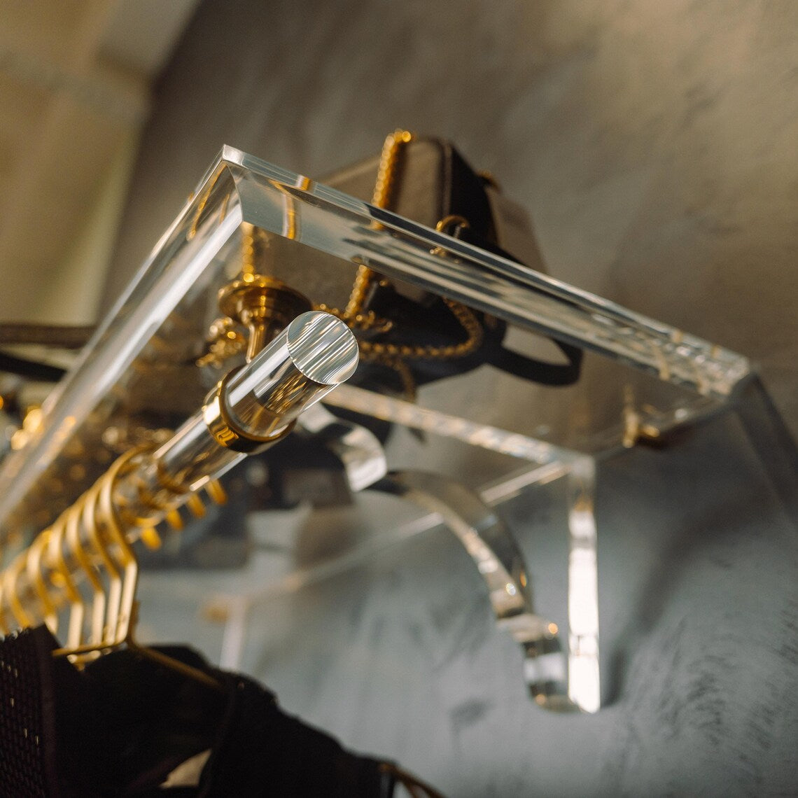 A clear acrylic wall-mounted floating clothing rack with gold accents