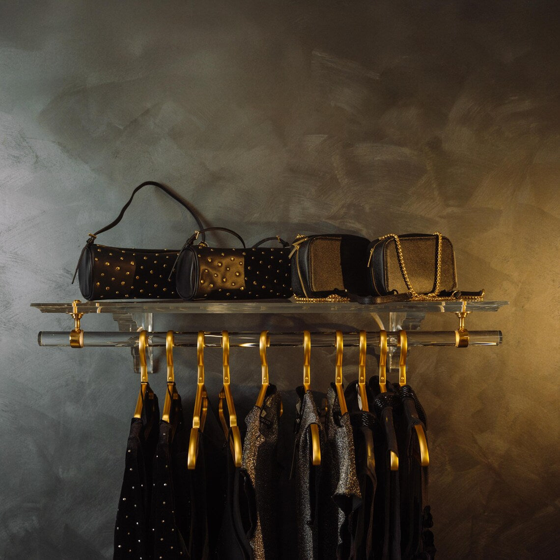 A clear acrylic wall-mounted floating clothing rack with gold accents
