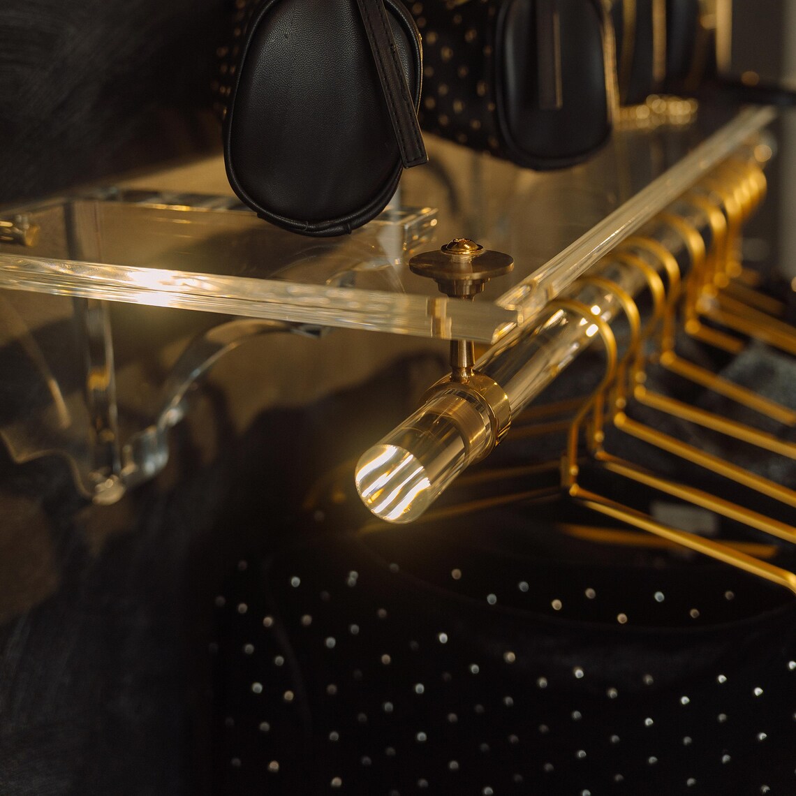 A clear acrylic wall-mounted floating clothing rack with gold accents