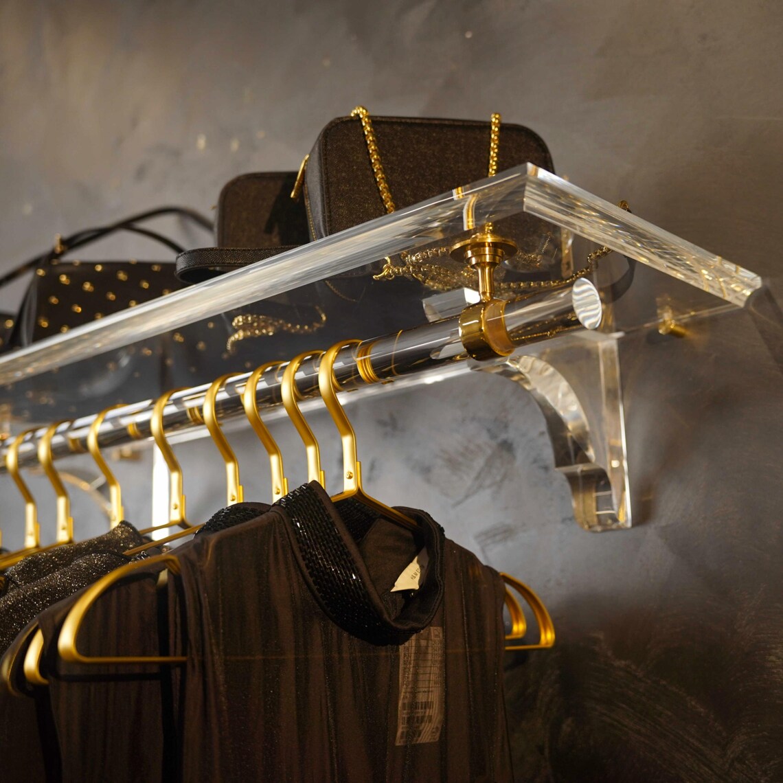 A clear acrylic wall-mounted floating clothing rack with gold accents