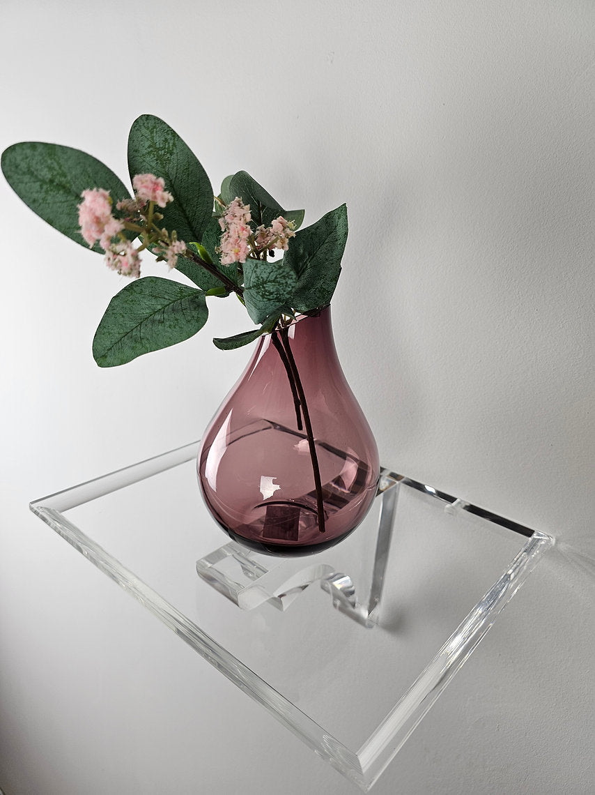 A clear acrylic floating shelf with a single mounting bracket