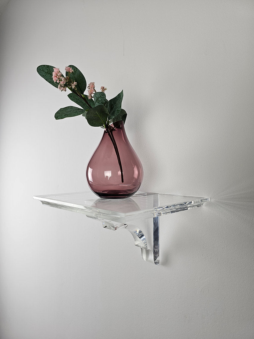 A clear acrylic floating shelf with a single mounting bracket