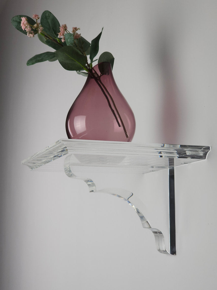A clear acrylic floating shelf with a single mounting bracket