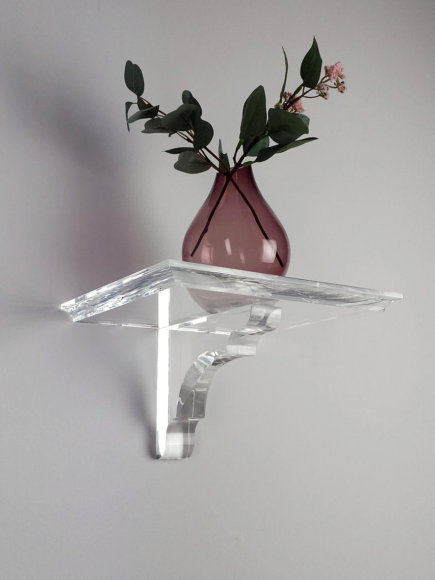 A clear acrylic floating shelf with a single mounting bracket