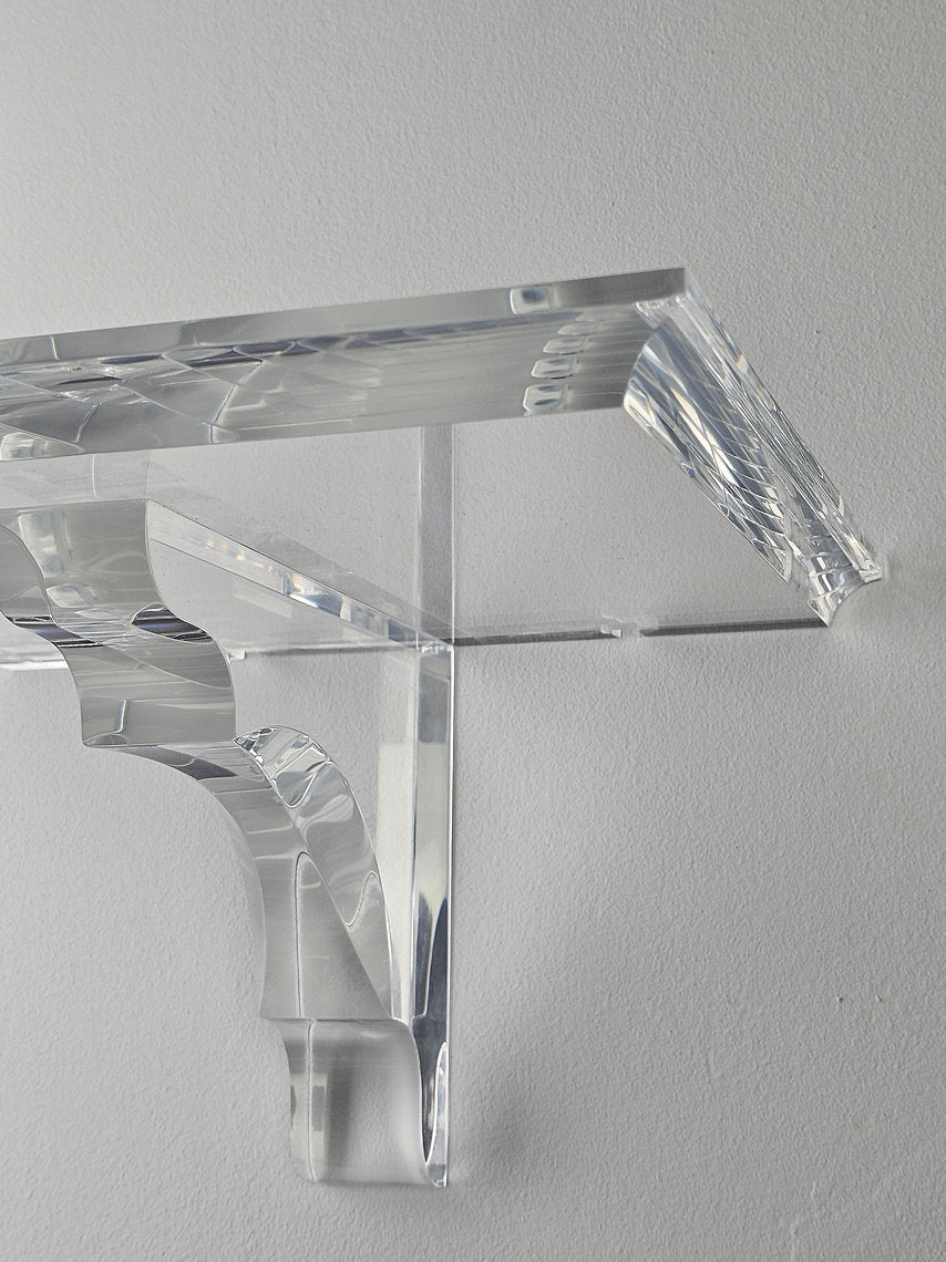 A clear acrylic floating shelf with a single mounting bracket