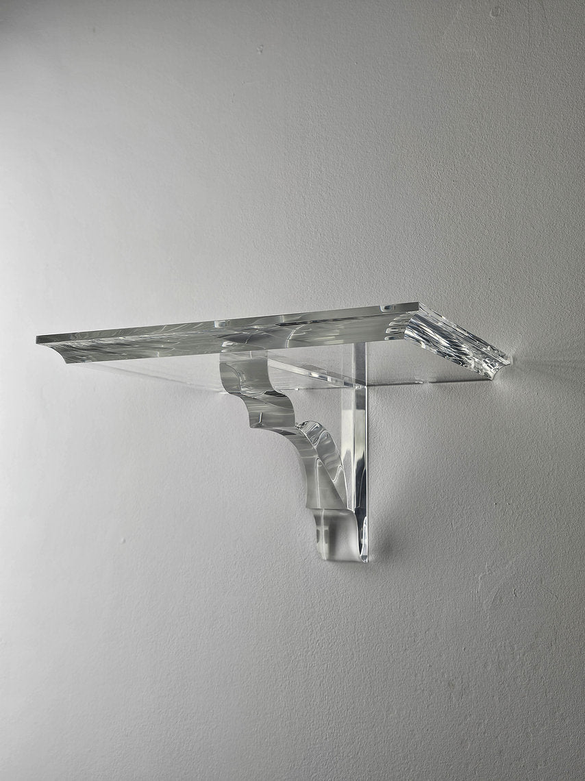 A clear acrylic floating shelf with a single mounting bracket