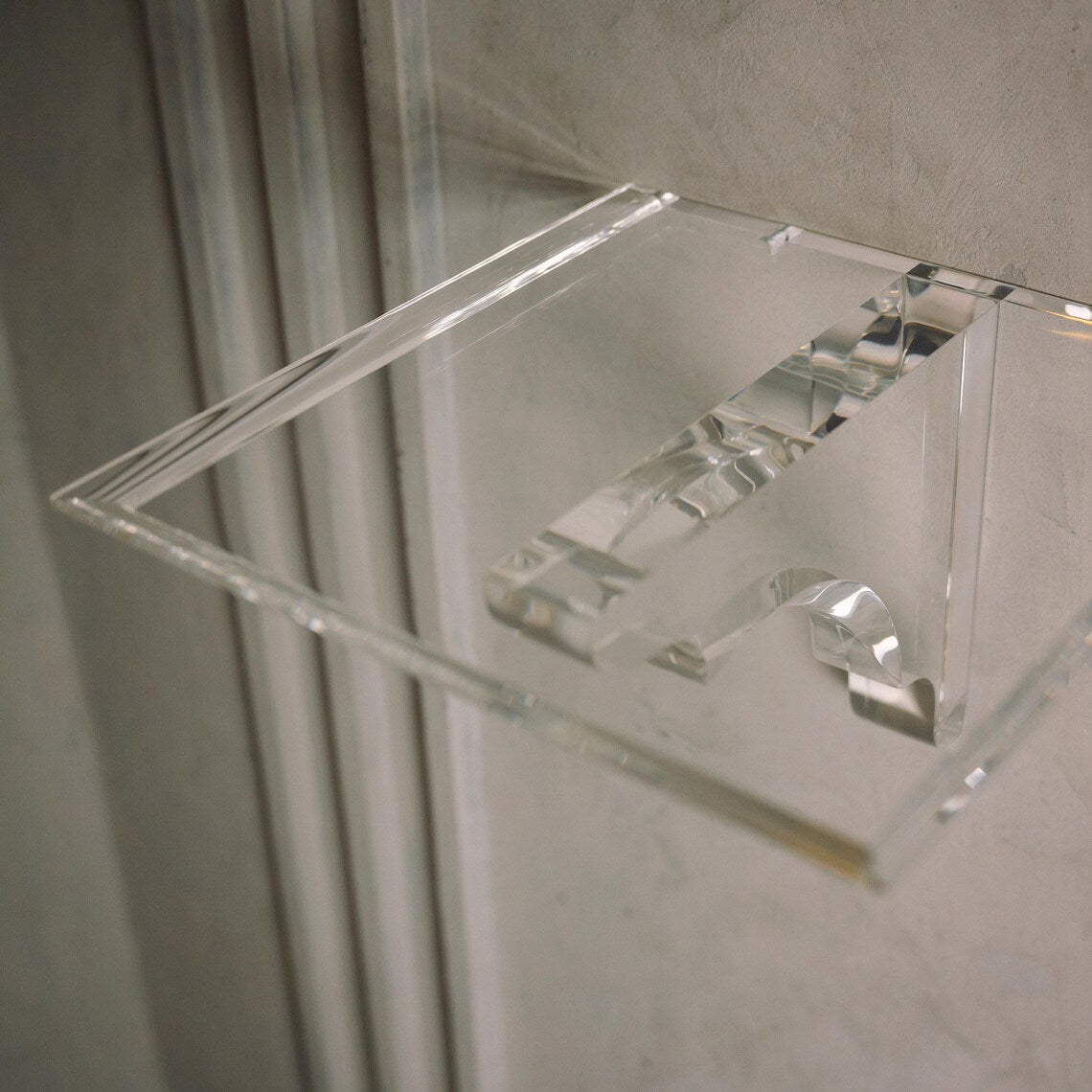 A clear acrylic floating shelf with a single mounting bracket
