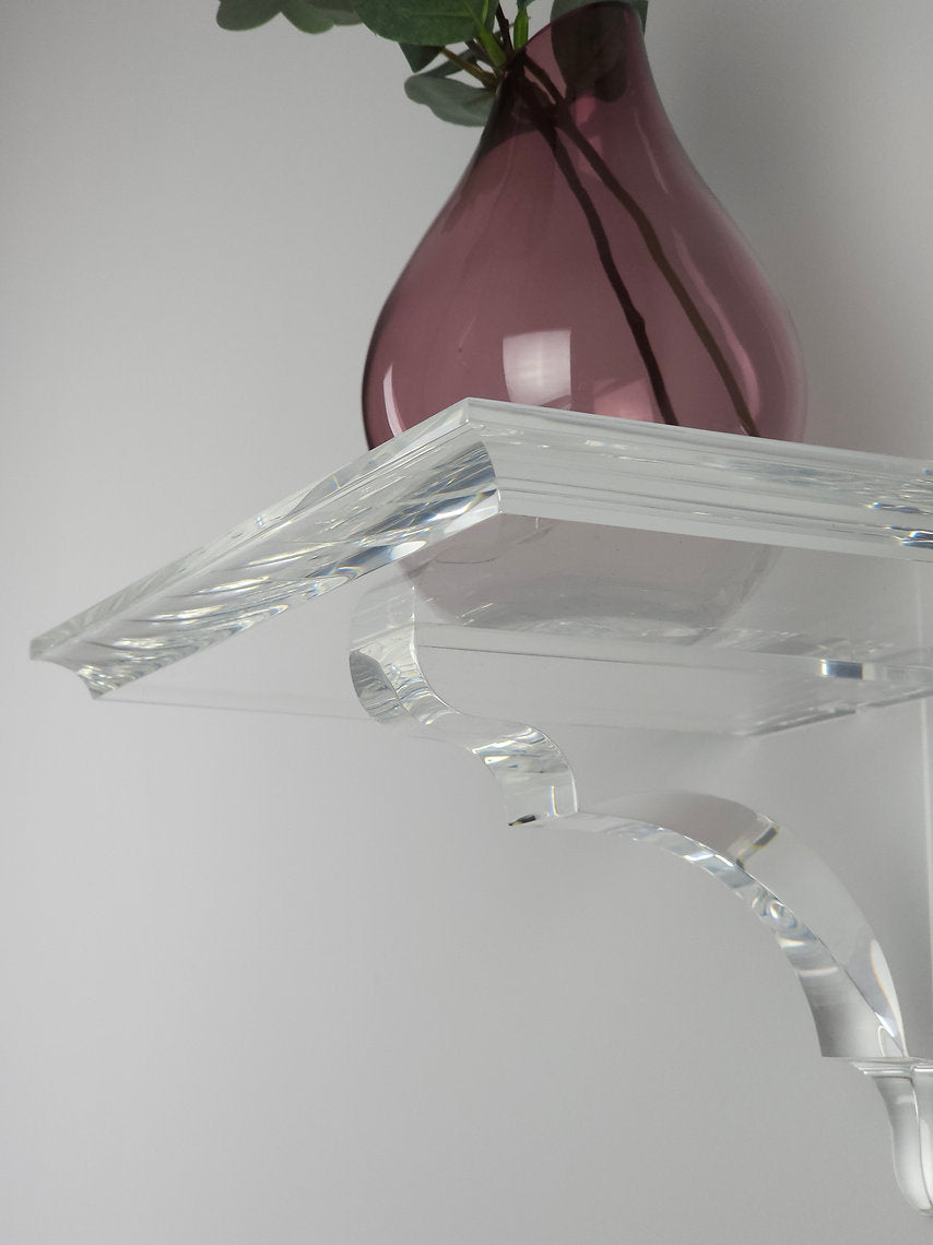 A clear acrylic floating shelf with a single mounting bracket